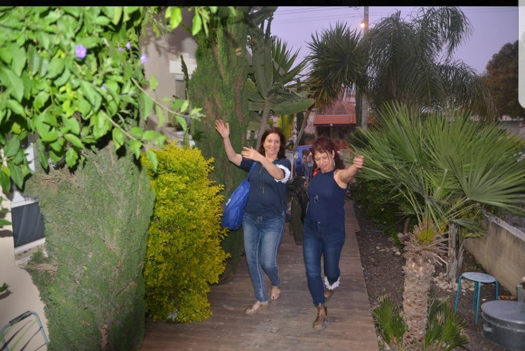 Two guests laughing and waving toward the camera as they arrive up Lili's garden path at dusk