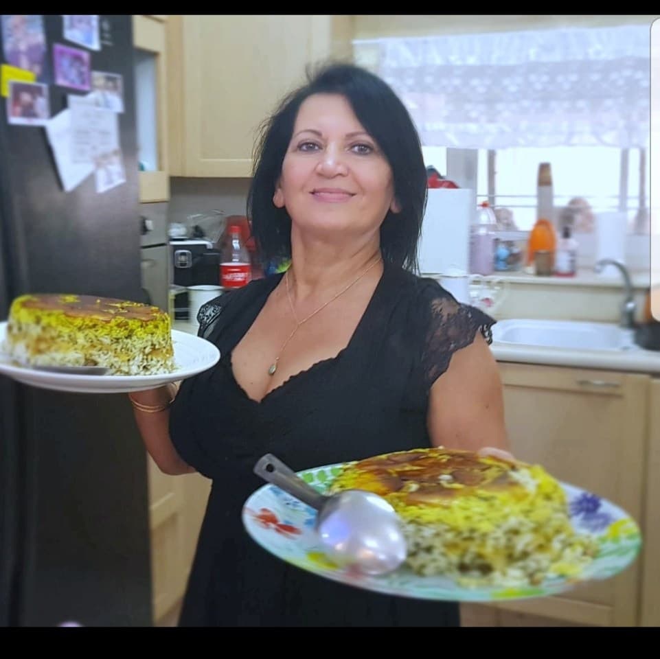 Lili Twizer smiling, holding two plates of saffron Persian rice with golden tahdig