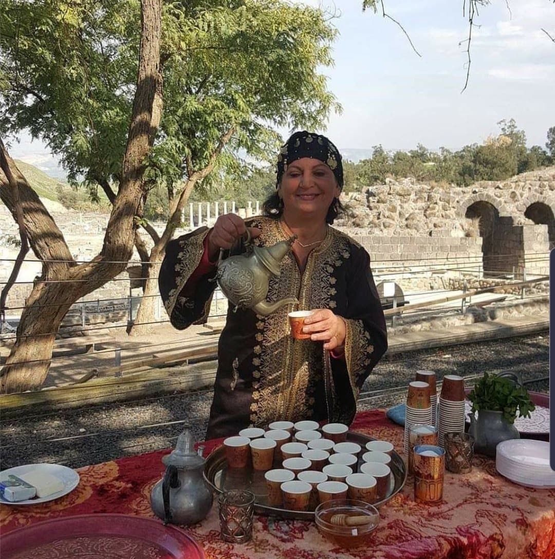 Lili Twizer in a traditional Persian dress pouring tea against the Roman ruins of Beit Shean