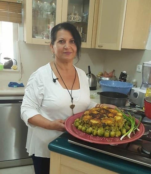 Lili Twizer smiling in her kitchen, holding a red platter of Persian rice with green peas and scallions